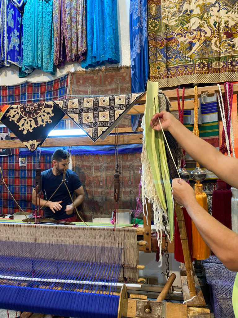 Man showing agave threads and a man working on a loom behind him