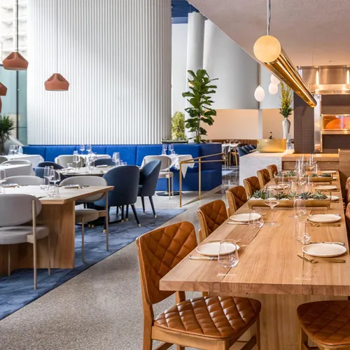 Inside of Blue Duck Tavern restaurant with tables along large windows and a wooden communal table in the center.