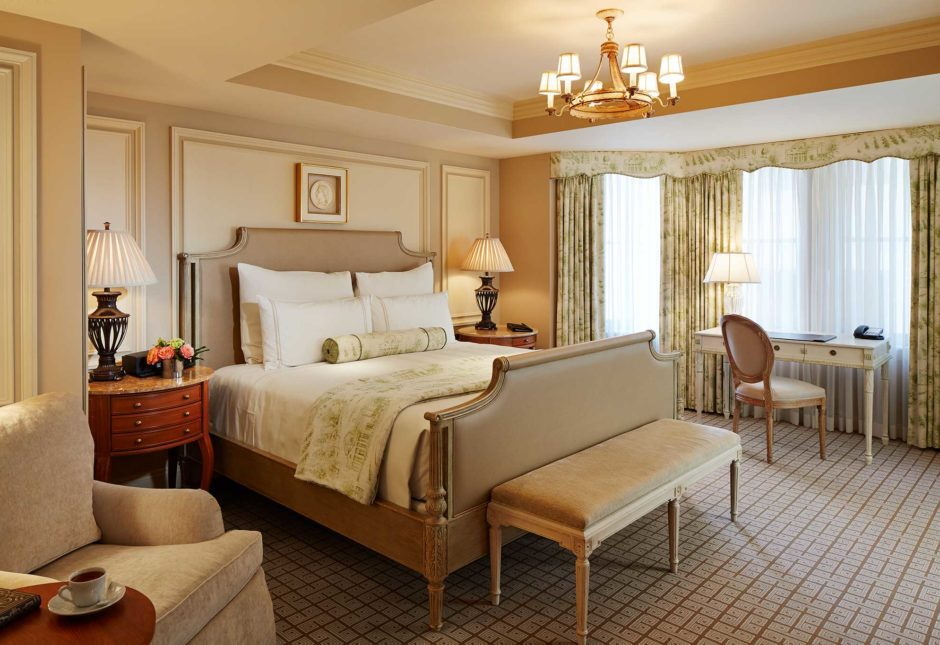 Elegant hotel room with bed, small desk, armchair, and bench