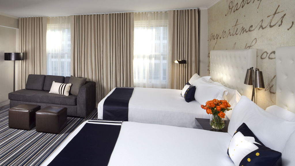 Inside of hotel room with two beds, a loveseat, and two large windows with curtains