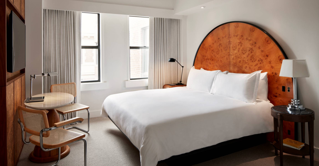 Stylish hotel room with bed and arched headboard, tv, table and chairs, and windows