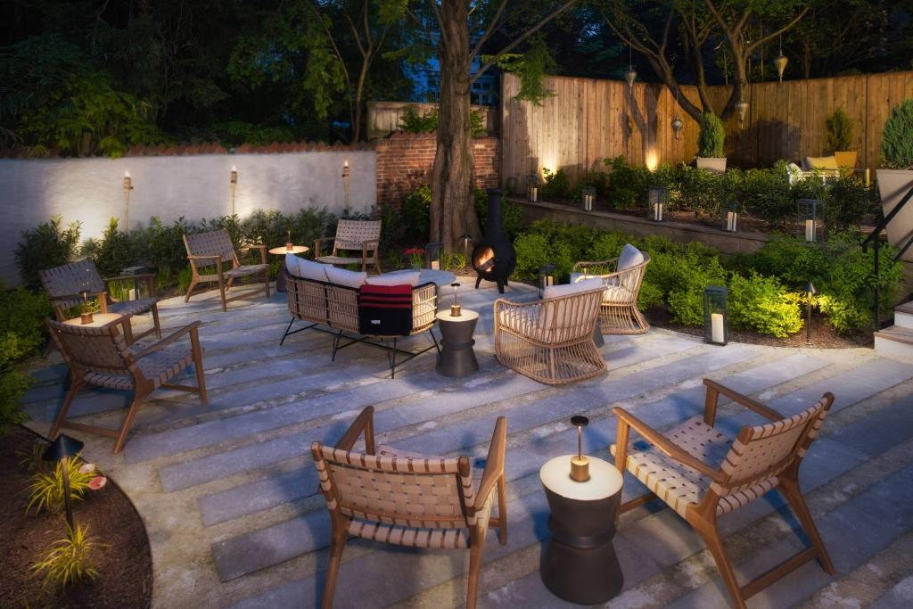 Outdoor garden patio with wicker chairs, greenery, and a stovepipe fireplace.