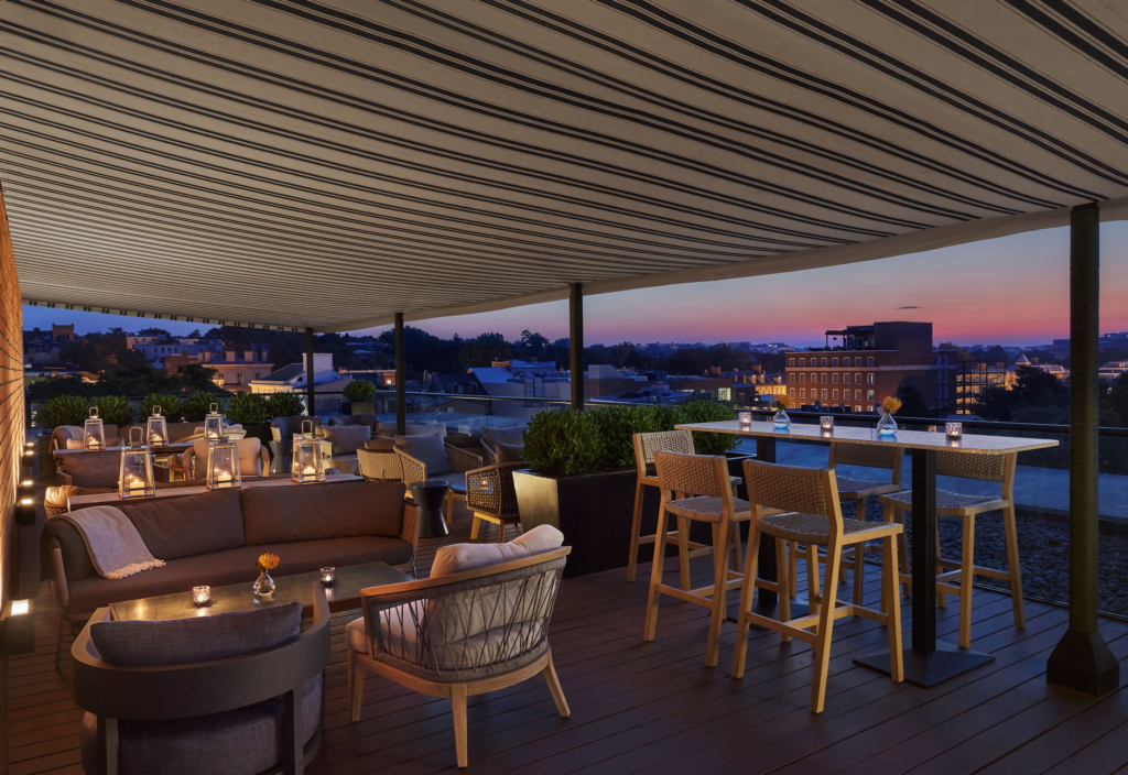 Covered outdoor rooftop patio with tall tables and sofas with sunset view of Washington DC