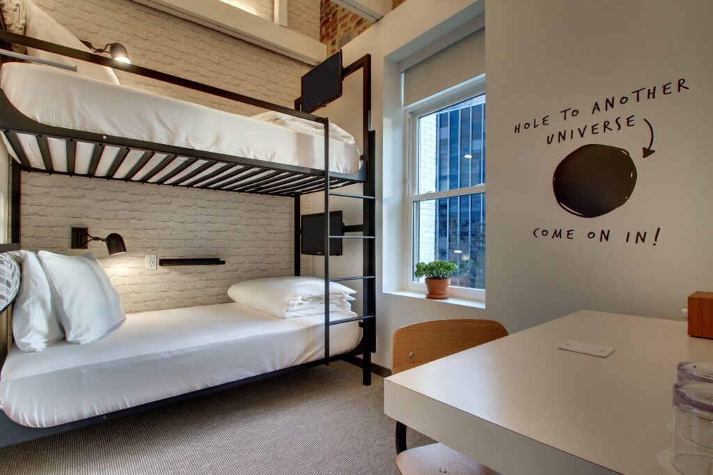 Inside of a small hotel room with bunk beds. a window, and a small writing desk.