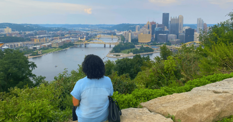 Woman sitting on a stone at an overlook of the city of Pittsburgh across the river