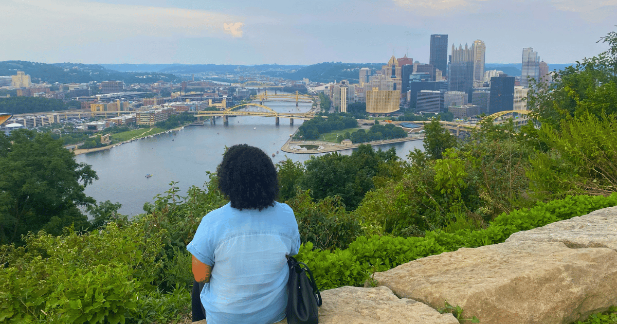 Woman sitting on a stone at an overlook of the city of Pittsburgh across the river