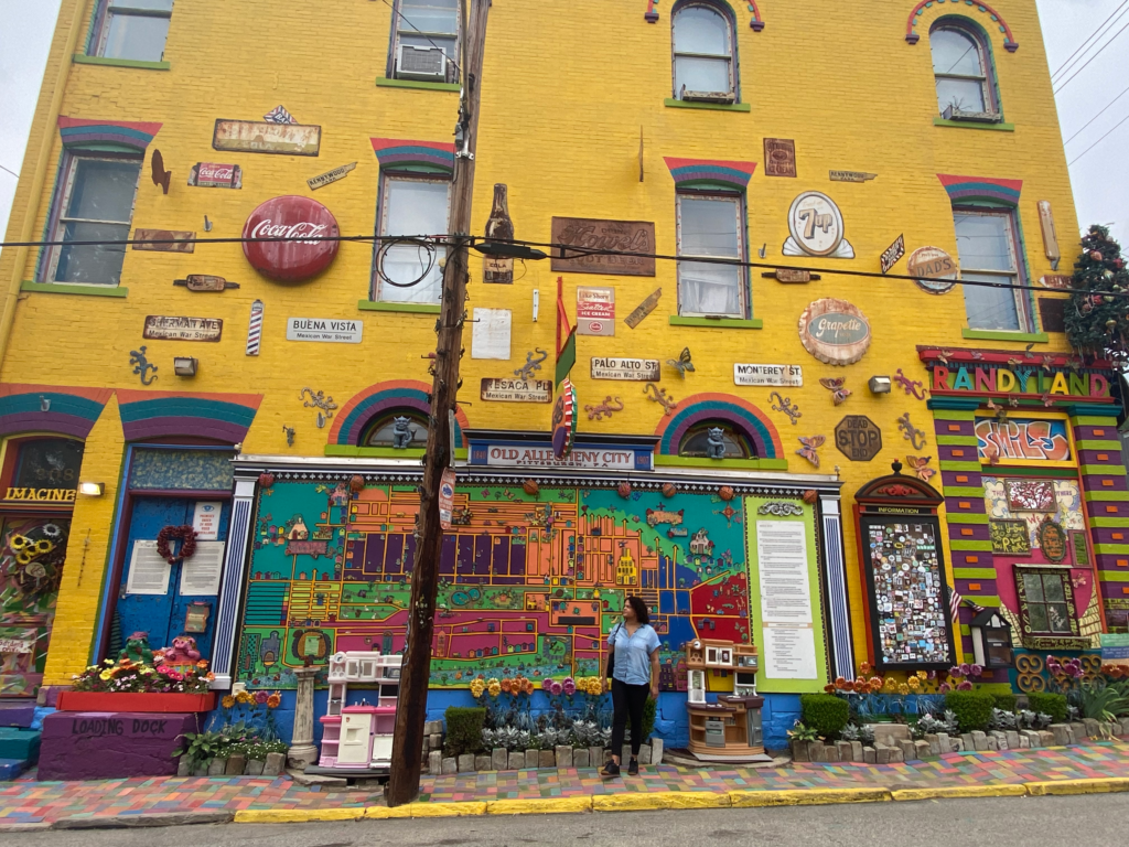 Woman standing at bus stop in front of colorful decorated yellow building