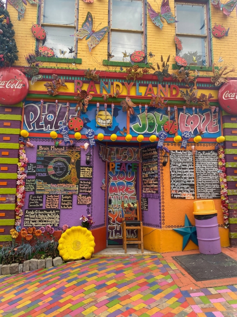 Front facade of a colorfully painted Pittsburgh row home with quirky decorations attached to it and a sign painted with the name Randyland